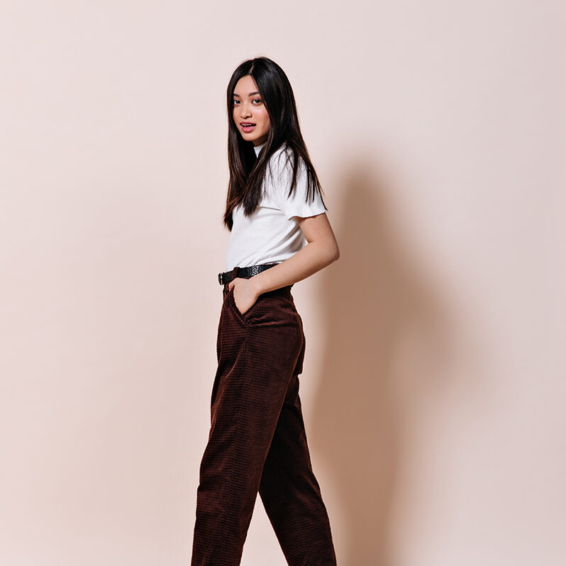 lady-with-long-hair-dressed-brown-pants-posing-beige-wall