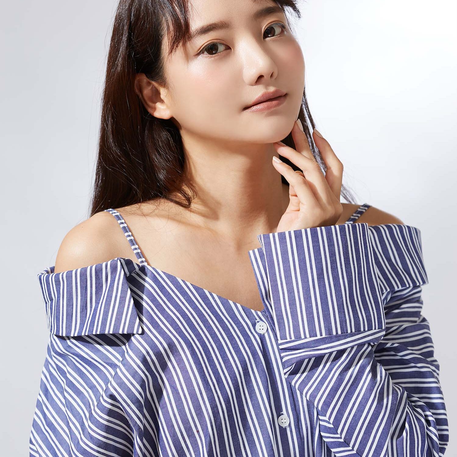 sensual asian woman in stylish pantsuit sitting in armchair and looking at camera on beige background